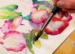 A hand holds a brush, painting vibrant flowers with watercolor on a canvas, blending colors skillfully.