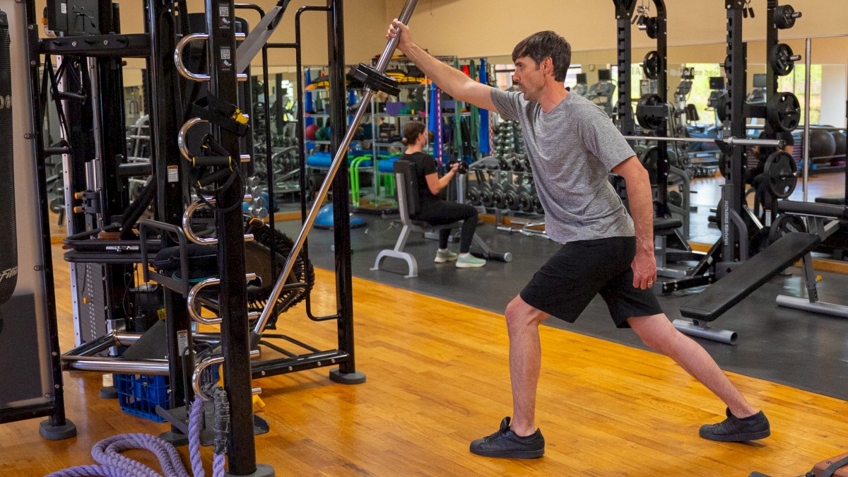 A person is exercising in a gym using ropes, surrounded by gym equipment and a wooden floor.