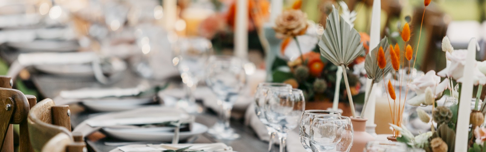 A beautifully set, elegant dining table with neatly arranged dinnerware, glassware, white napkins, and vibrant floral decorations with candles.