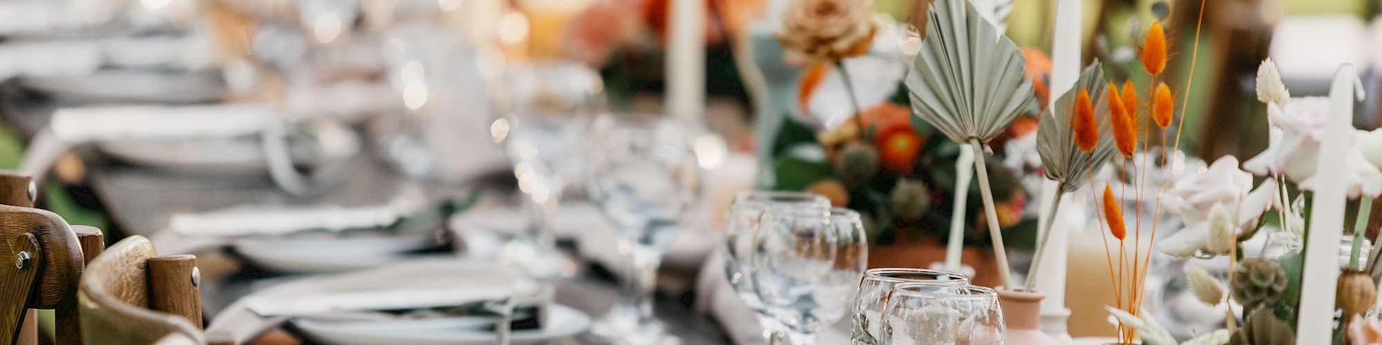 A beautifully set, elegant dining table with neatly arranged dinnerware, glassware, white napkins, and vibrant floral decorations with candles.