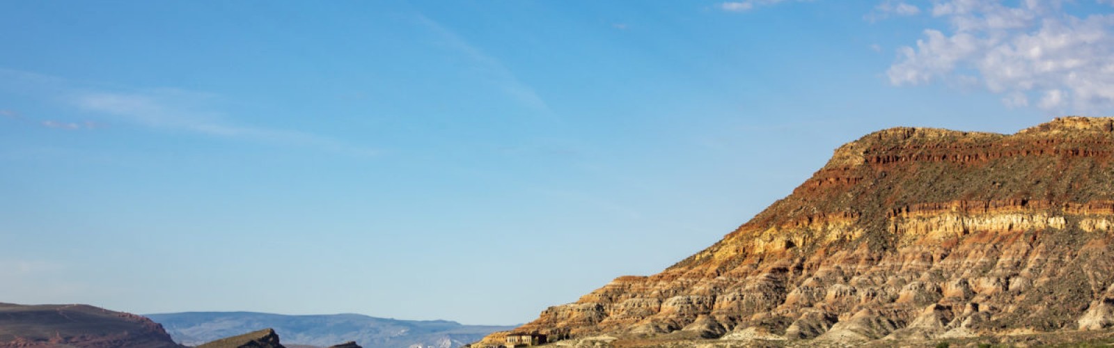 Two people are paddleboarding on a calm lake with a rocky landscape and hills, under a blue sky with scattered clouds.