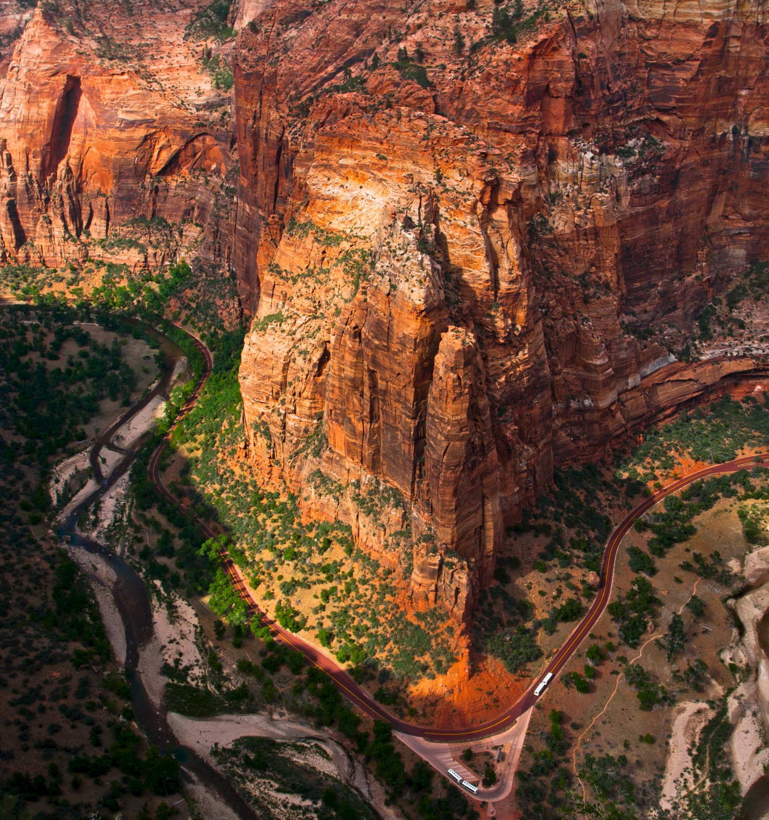 A winding road and river cutting through a vibrant red-rock canyon landscape with lush greenery.