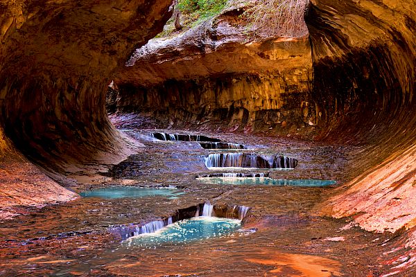 This image depicts a natural rock formation featuring cascading waterfalls and reflective pools, creating a serene and colorful scene.