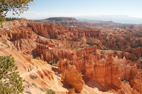 The image shows Bryce Canyon National Park's stunning red rock formations and hoodoos under a clear sky, with several people hiking on a trail.