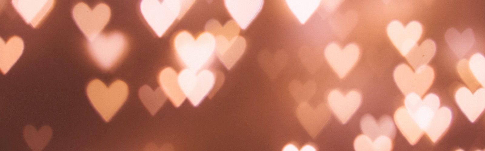The image shows a bokeh effect with glowing heart shapes in soft, warm tones against a darker background. The hearts vary in size and brightness.