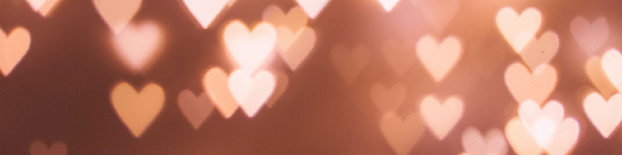 The image shows a bokeh effect with glowing heart shapes in soft, warm tones against a darker background. The hearts vary in size and brightness.