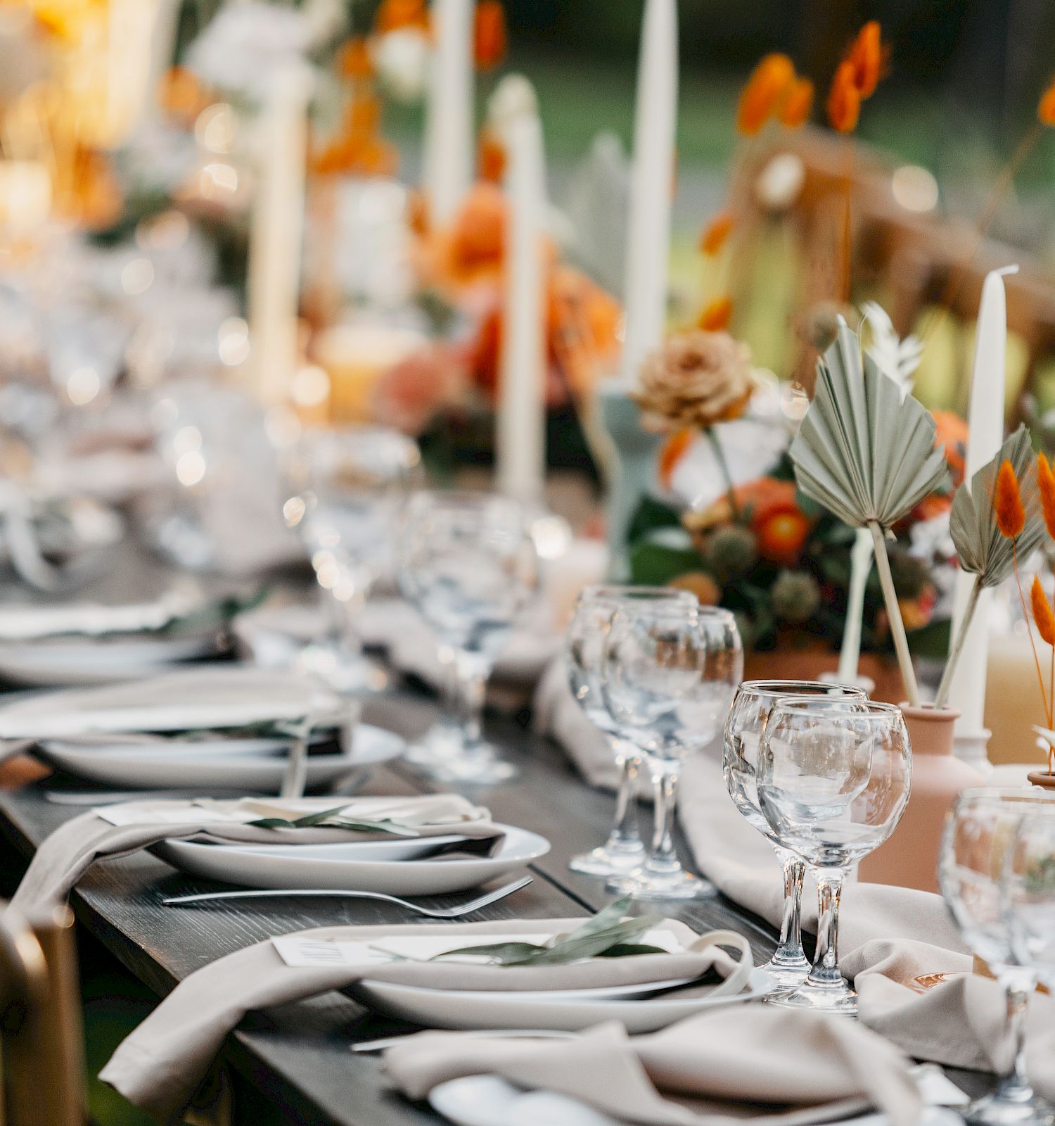 A beautifully set dining table with elegant glassware, plates, floral arrangements, and candles, ready for an outdoor event or celebration.