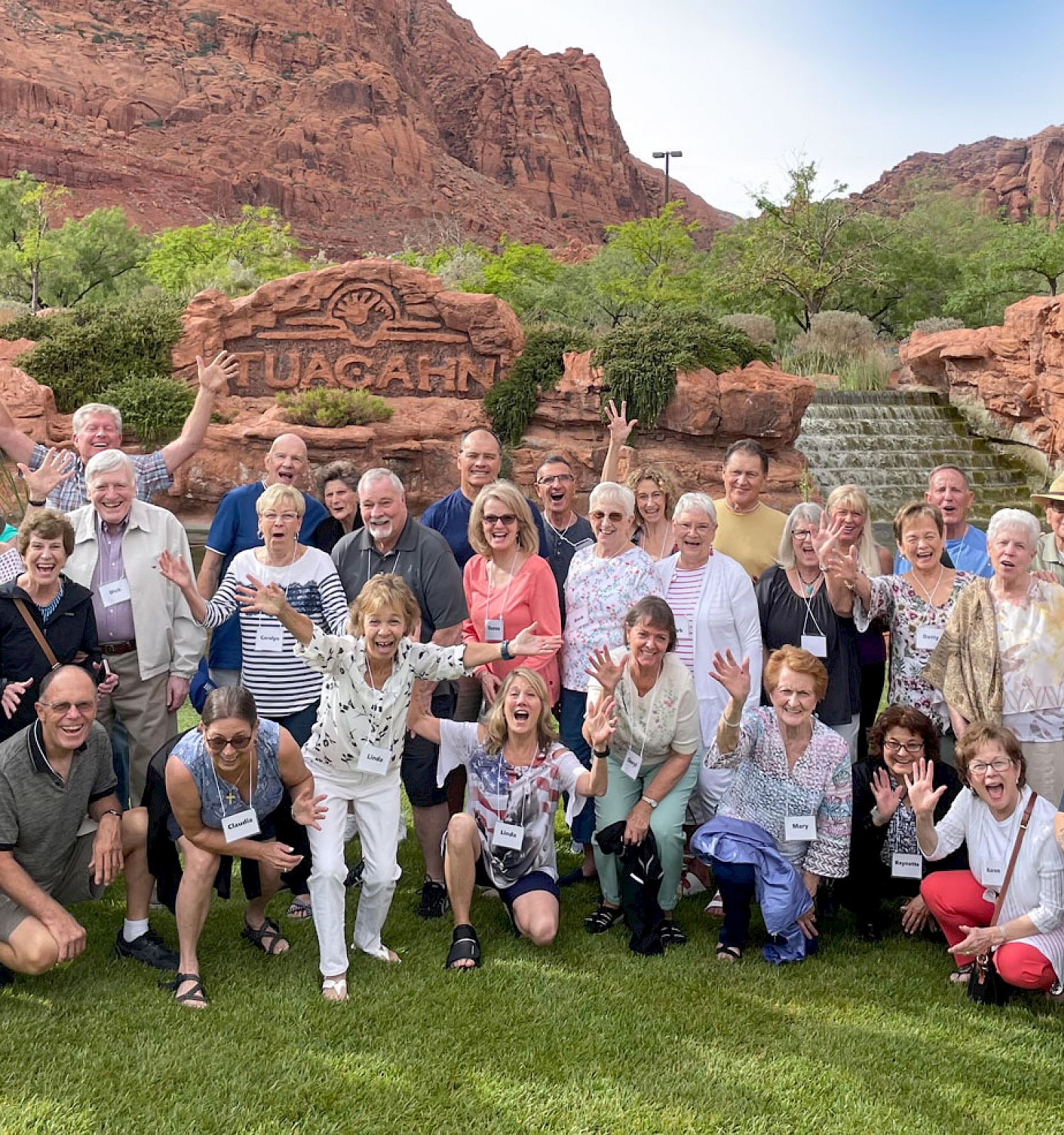 A large group of people posing outdoors in front of a rock formation and sign that reads 