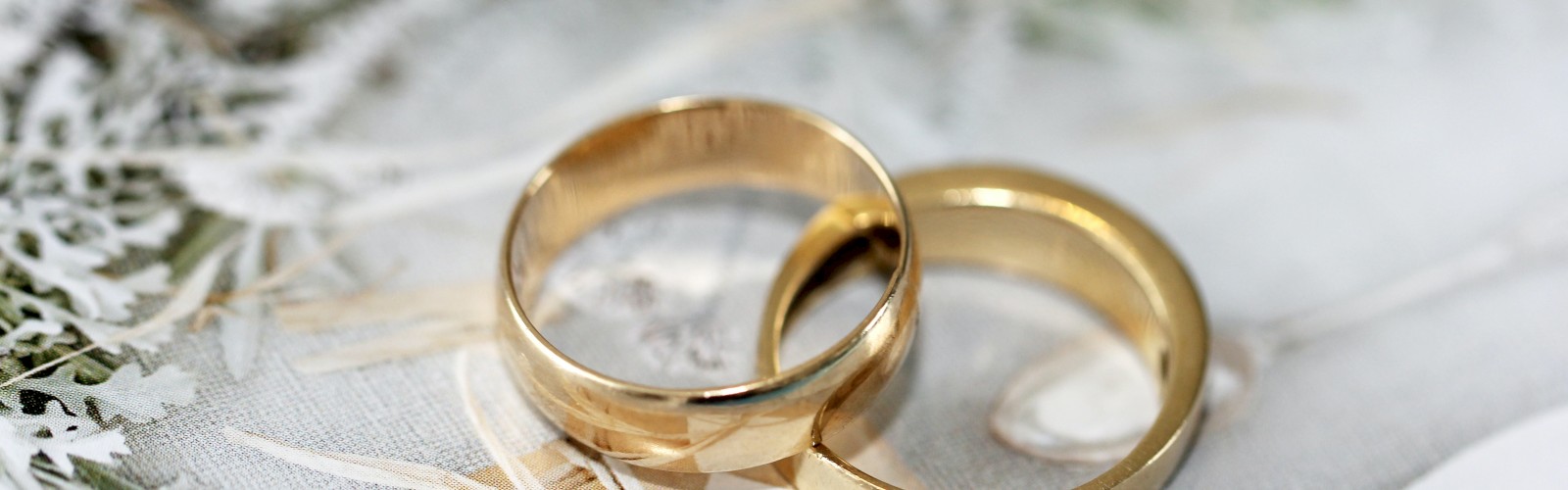 Two gold wedding rings placed together on a decorative surface with leaves and paper.