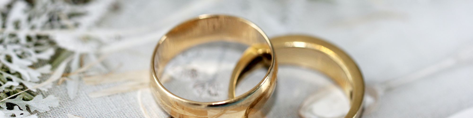 Two gold wedding rings placed together on a decorative surface with leaves and paper.