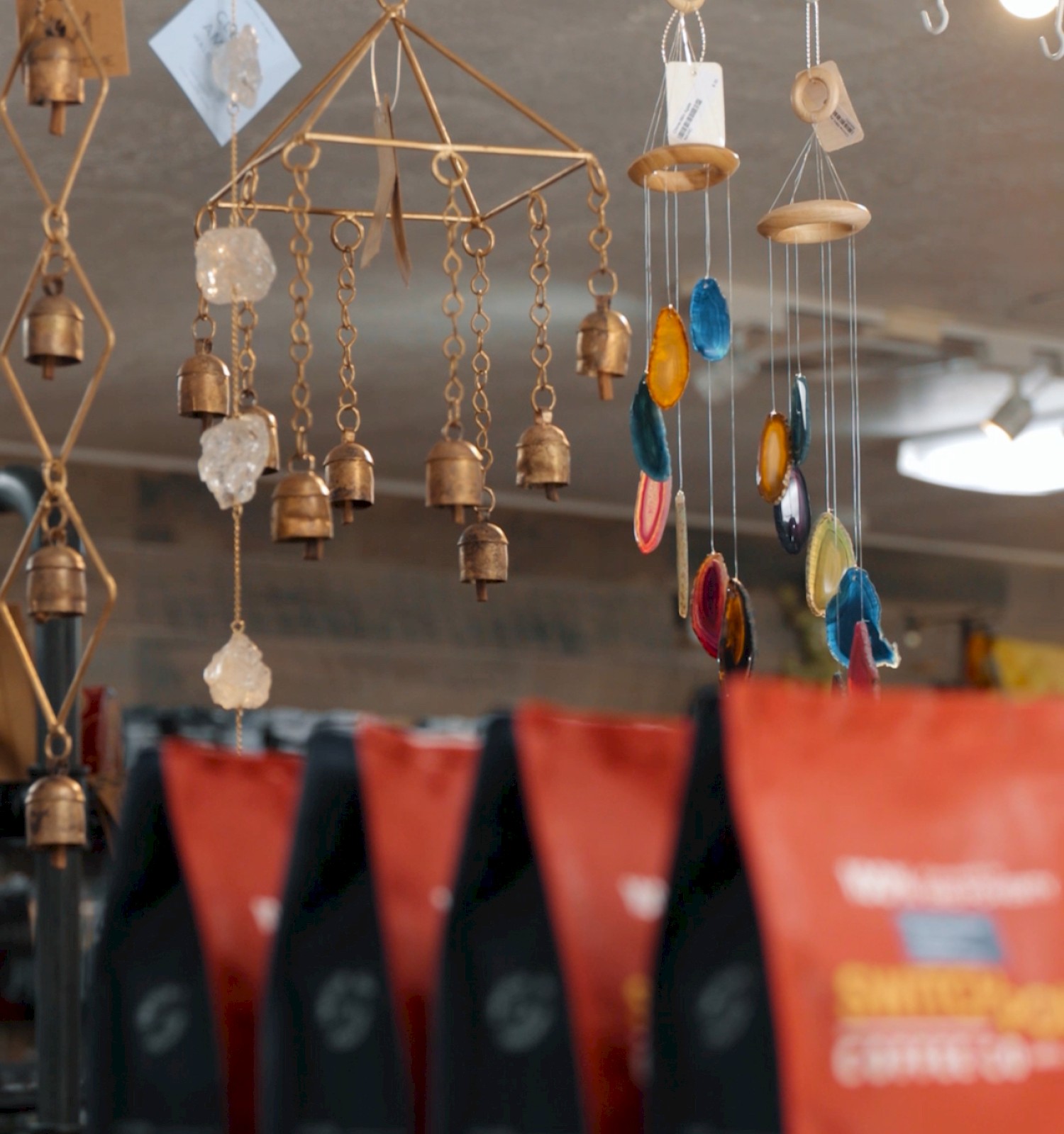The image shows hanging decorative items, including bells and ornaments, with bags of coffee in the foreground on a shelf.