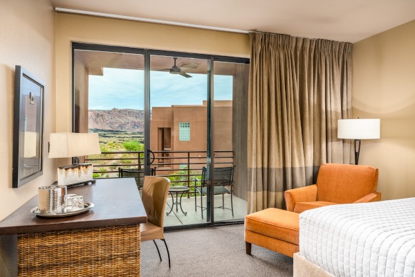 A cozy hotel room with a bed, an orange chair, and a desk, featuring a balcony with a scenic outdoor view.