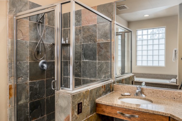A modern bathroom featuring a glass-enclosed shower, slate tiles, a granite countertop sink, and a window.