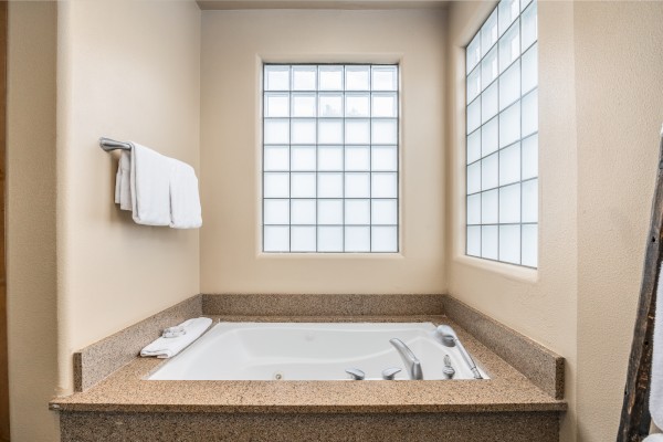 The image shows a bathroom with a bathtub, beige walls, glass block windows, and towels neatly hung above the tub.