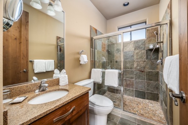 A bathroom with a stone-tiled shower, sink, and toilet. Neutral colors create a clean, modern look with towels neatly placed.