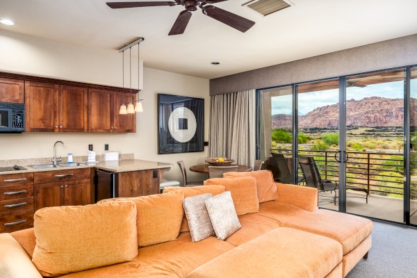 A cozy living area with an orange couch, kitchen, dining table, and large windows overlooking a scenic mountain view.