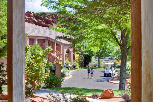 The image shows a porch view with a bench, trees, and a street outside. There are people walking and a golf cart in the background.