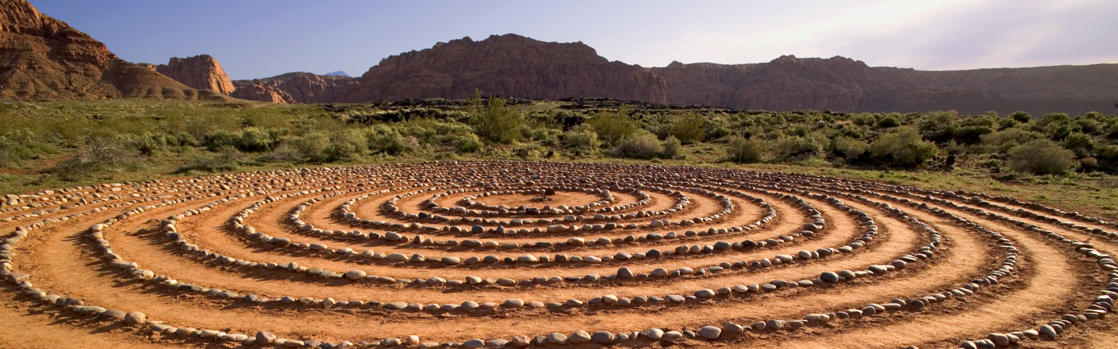 A spiral rock formation on dirt in a natural outdoor setting with mountains and greenery in the background.