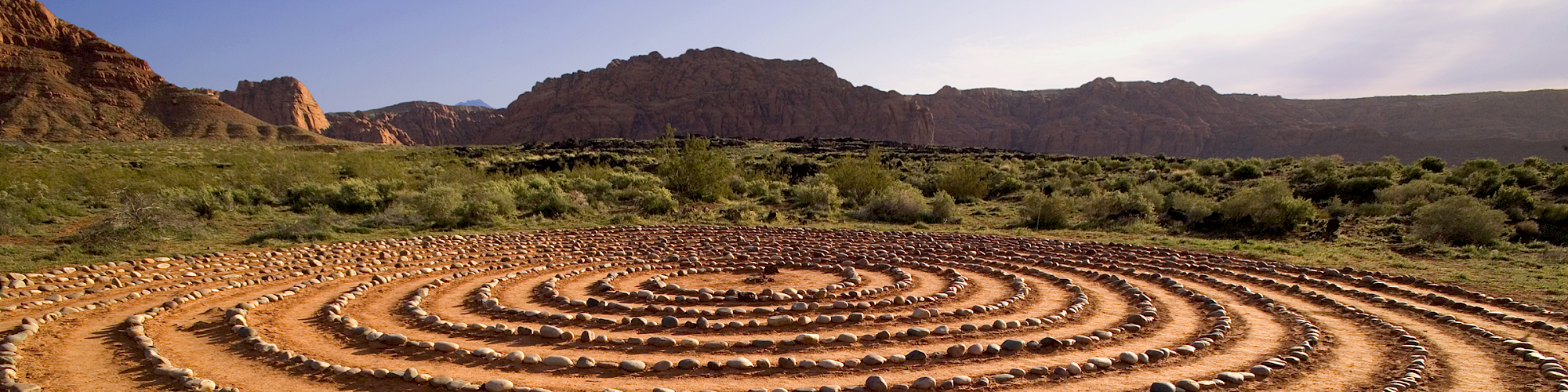 A spiral rock formation on dirt in a natural outdoor setting with mountains and greenery in the background.